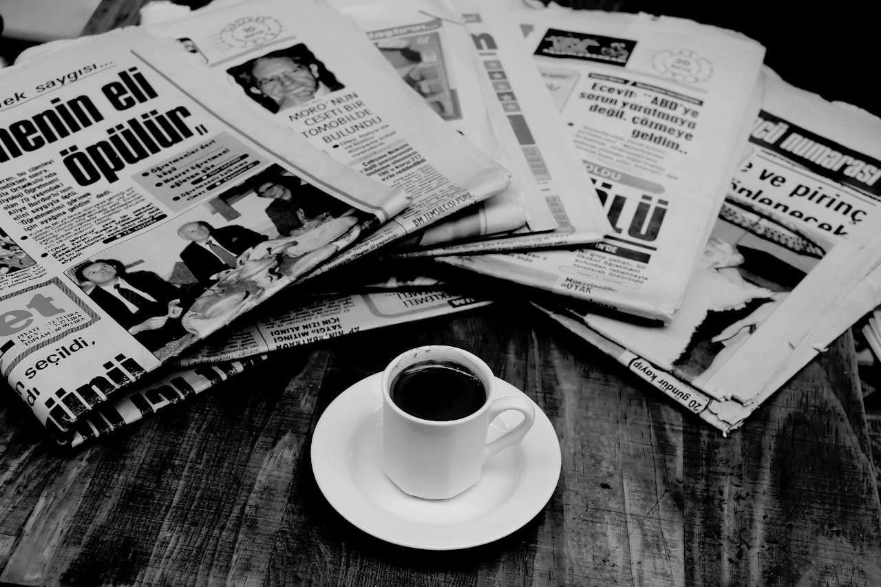 portfolio-02 A cup of Turkish coffee sits on a wooden table next to a stack of newspapers.