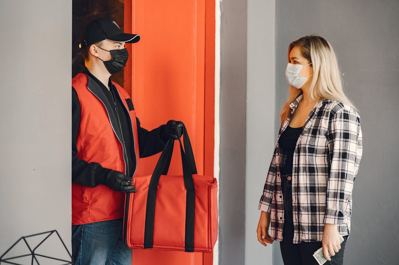 cta-02 Masked delivery person handing food to customer during pandemic.