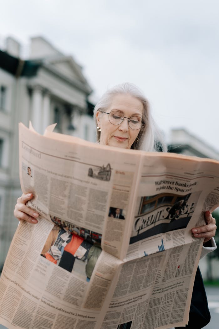 portfolio-06 Senior woman with glasses enjoying reading a newspaper outdoors. Perfect for lifestyle themes.