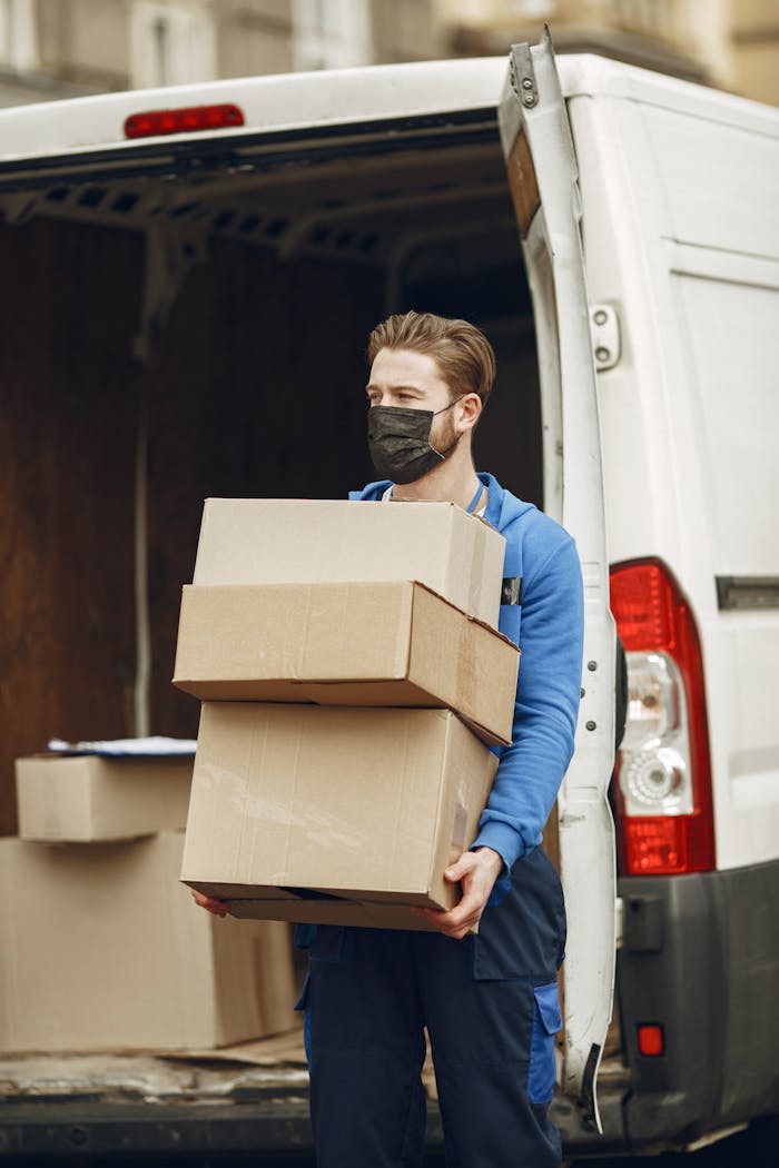 portfolio-01 Man wearing mask delivering cardboard boxes from van outdoors.