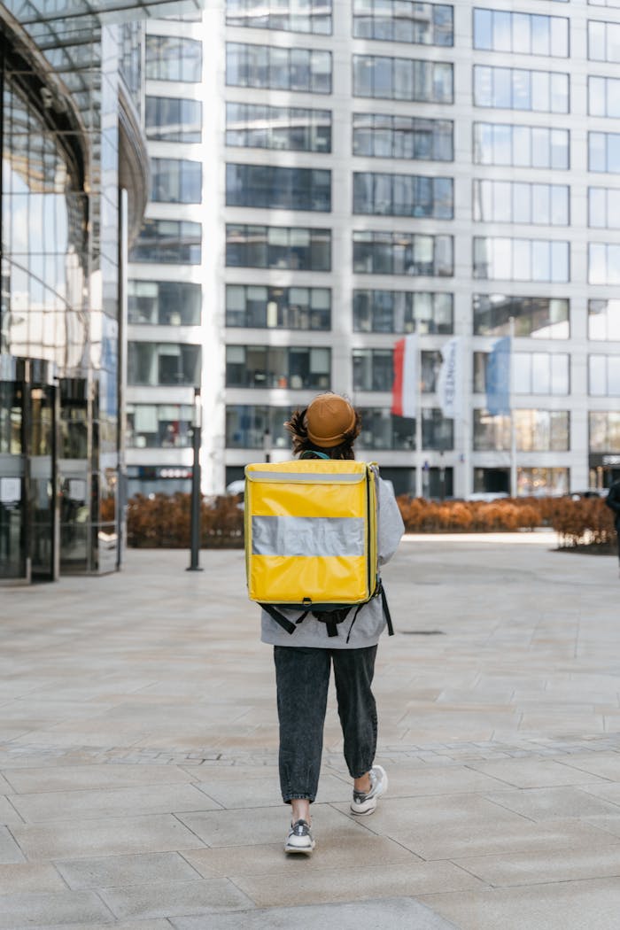 gallery-06 A food delivery person walking downtown with a yellow thermal bag, showcasing urban courier service.